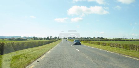 Photo for Rear view of cars driving on motorway, Ireland. Road with metal safety barrier or rail. cars on the asphalt under the cloudy blue sky. Highway traffic. - Royalty Free Image