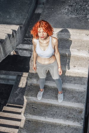 Foto de Mujer en ropa de correr, top y pantalones cortos, estirando su cuerpo y preparándose para una carrera, o enfriándose después del ejercicio - Imagen libre de derechos