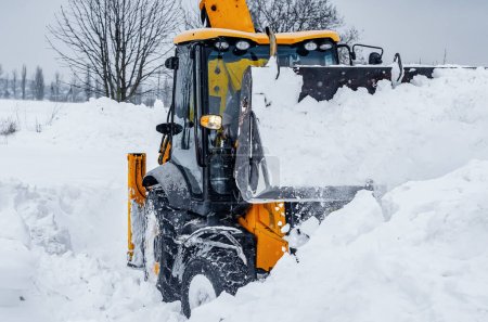 Foto de Gran tractor amarillo limpia la nieve de la carretera. Limpieza y limpieza de carreteras en la ciudad de la nieve en invierno - Imagen libre de derechos