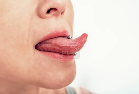 Foto de Perforación en la lengua de la mujer. Vista lateral de la boca de la mujer con la lengua sobresaliendo. - Imagen libre de derechos