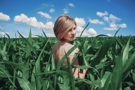 Photo for Young Woman Standing in a Green Cornfield with an Exposed Back, Smiling and Enjoying the Outdoors - Royalty Free Image