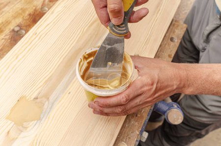 Foto de Carpenter utiliza masilla para alisar los nudos en una tabla de madera. Fondo de recuperación. - Imagen libre de derechos