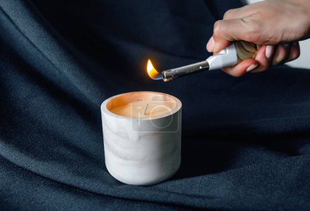 Téléchargez les photos : Éclairage d'une bougie parfumée décorative avec un briquet sur fond noir. Aromatisation des locaux huiles essentielles - en image libre de droit