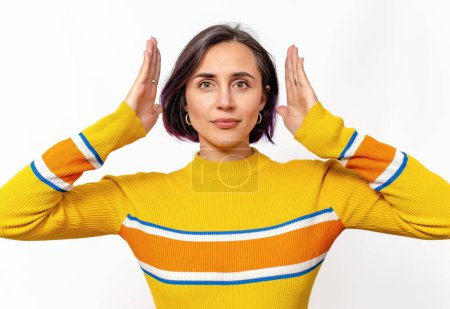 Foto de Mujer tranquila seria confiada que usa suéter amarillo aislado sobre fondo blanco. Manos cerca de la cabeza - Imagen libre de derechos