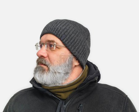 Stylischer ernster Mann mit grauem Bart und Schnurrbart im Winterhut. Er schaut weg. Weißer Hintergrund