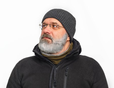 Stylish serious man with gray beard and mustache in winter hat. He looks away. White background