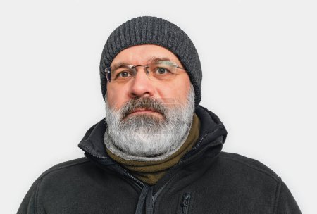 Serious man with gray beard and mustache in winter hat. Looks into camera. White background