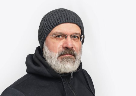 Seriöser Mann mit grauem Bart und Schnurrbart in Wintermütze. Blickt in die Kamera. Weißer Hintergrund