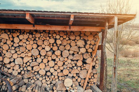 Gleichmäßig gehäckseltes Brennholz unter einem Vordach in der Nähe des Hauses gestapelt