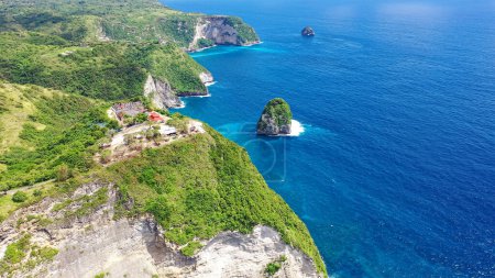 Blue sea washes rocky mountains covered forest. Separate rocks in water. Nusa Penida Indonesia