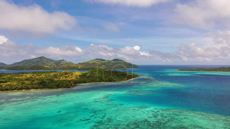 Turquoise ocean waters under the clouds. Mountains in the distance. Drone view of Fiji Islands.