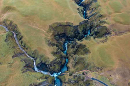 Between the hills in Iceland flows winding blue river, branch of mountain streams. View from drone
