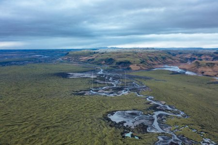Scenic canyon and winding frozen river in cloudy weather with green grass and moss. East Iceland