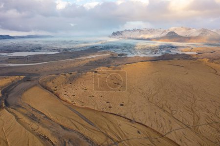 Cloudy sunset drone view mountain peaks covered with snow. Volcanic valley below. East Iceland.