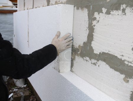 Photo for House exterior wall foam insulation. A close-up of a building contractor installing a rigid foam, styrofoam insulation on the concrete block house wall. - Royalty Free Image