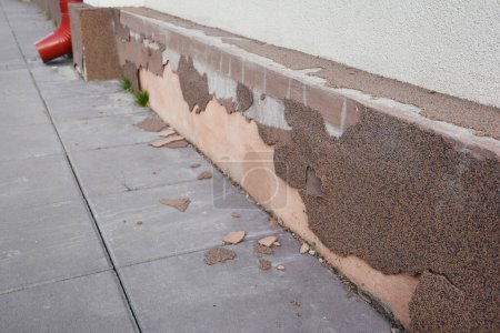 Facing with decorative plaster  house foundation repair - warning signs. House foundation repair caused by damp from rain gutter downspout pipe in problem area. Plinth foundation repair.