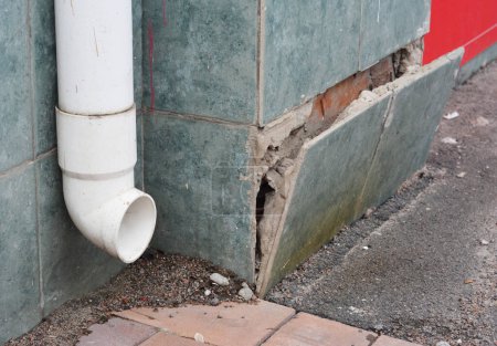 Photo for House foundation facing with ceramic tiles. House foundation repair caused by damp from rain gutter downspout pipe in problem area. Plinth foundation repair. - Royalty Free Image