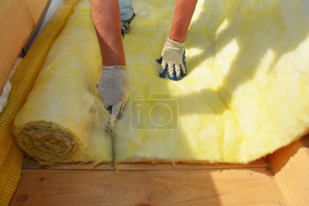 Foto de Roofer contratista aislante techo de la casa y el corte de lana mineral con un cuchillo. Aislamiento de la casa durante la construcción del techo. - Imagen libre de derechos