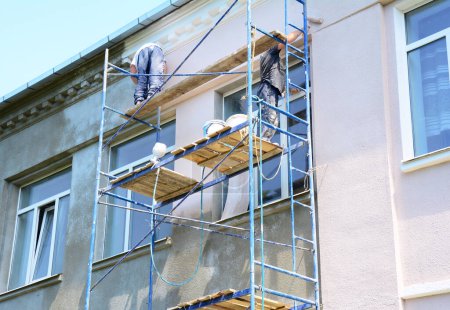 Foto de Contratistas pintando paredes fuera de la fachada de la casa. Primer plano en la pintura de la pared exterior de la casa durante la renovación de la casa. - Imagen libre de derechos