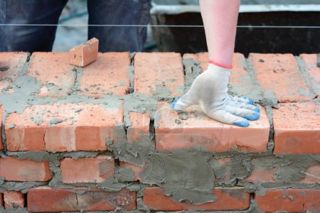A mason person is building brick house wall. Close up on half bat and quarter brick on house brick wall construction.