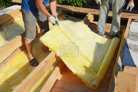 Isolation grenier avec laine minérale. L'entrepreneur de toiture mesure le matériau d'isolation de laine minérale pour couper pendant l'isolation du plancher du grenier.