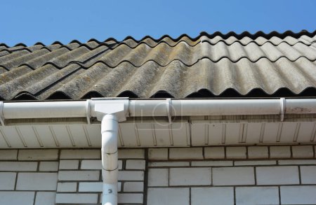 Foto de Casa de ladrillo blanco con láminas de techo de asbesto viejas y nuevas reparadas y tubería de canaleta de lluvia de plástico. - Imagen libre de derechos