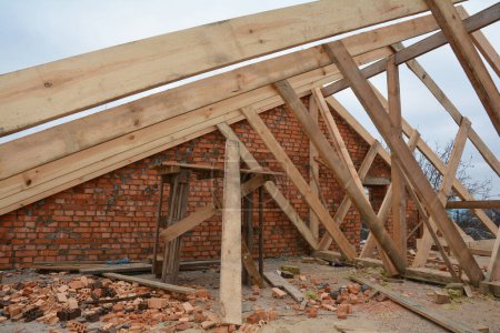 Foto de Wood framing during the roofing construction.Timber trusses, roof framing with a close-up of roof beams, struts and rafters against a brick wall. - Imagen libre de derechos