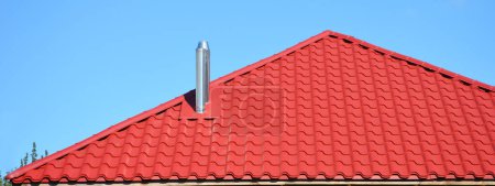 Photo for A close-up of a red metal roof with coaxial chimney, stainless steel metal chimney, flue pipe against the blue sky. - Royalty Free Image