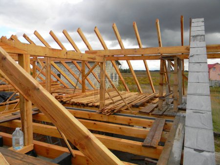 Téléchargez les photos : Construction de toiture : un gros plan sur une charpente de toit inachevée avec solives de plafond en bois, poutres de toit, sous-paillettes, chevrons et fermes installés. - en image libre de droit