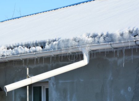 Photo for Frozen gutters damage. House  roof covered snow, icicles and frozen roof gutter with downspout pipe. - Royalty Free Image