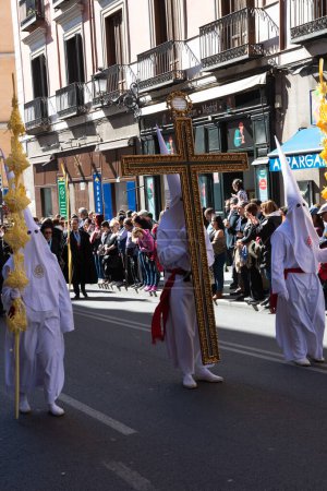 Foto de Madrid, España; 2 de abril de 2023: Procesión de la Semana Santa del Domingo de Ramos, coloquialmente llamada "el borriquito" .Miembros vestidos de blanco con capuchas, togas y cruz - Imagen libre de derechos