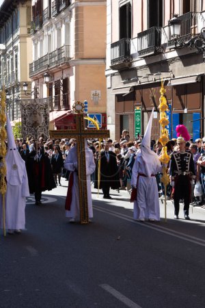 Foto de Madrid, España; 2 de abril de 2023: Procesión de la Semana Santa del Domingo de Ramos, coloquialmente llamada "el borriquito". Miembros vestidos de blanco con capuchas y batas con la cruz y las palmas. - Imagen libre de derechos