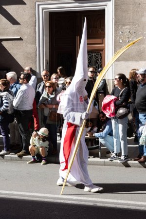 Foto de Madrid, España; 2 de abril de 2023: Procesión de la Semana Santa del Domingo de Ramos, coloquialmente llamada "el borriquito". Miembro vestido de blanco con capuchas, toga y una hoja de palma seca. - Imagen libre de derechos