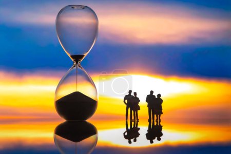 Photo for Miniature people. silhouettes of different people watching the sunset next to the hourglass. end of life. - Royalty Free Image