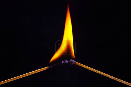 Téléchargez les photos : Allumette brûlante sur un fond noir. Chaleur et lumière de la flamme du feu - en image libre de droit
