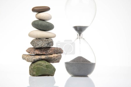 pyramid of stacked stones and hourglass on a white background. stabilization and balance in life