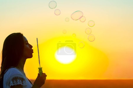 Photo for Woman blows bubbles against the backdrop of the setting sun. summer fun and outdoor recreation - Royalty Free Image
