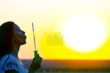 Photo for Woman blows bubbles against the backdrop of the setting sun. summer fun and outdoor recreation - Royalty Free Image