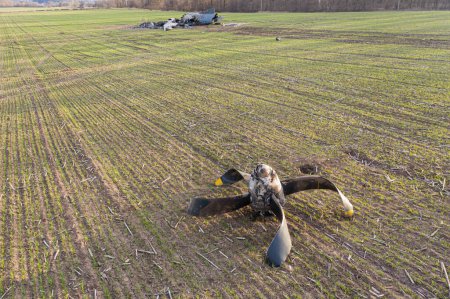 En esta foto, se puede ver un avión AN-26 tumbado en un campo en Ucrania después de un accidente. El avión parece haber sufrido daños significativos, con partes dispersas alrededor de los restos y