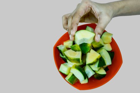 Téléchargez les photos : Petite paix de papaye verte dans un bol orange Un morceau de papaye dans une main, isolé sur fond gris - en image libre de droit