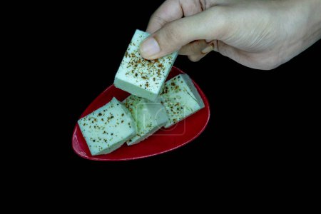 Téléchargez les photos : Kharvas dans une petite assiette rouge, Ramassage à la main d'une pièce, Kharvas est un produit laitier doux, isolé sur fond noir - en image libre de droit