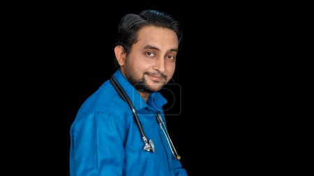 Téléchargez les photos : Vue transversale du côté gauche du jeune médecin masculin sud-asiatique tenant un stéthoscope sur l'épaule isolée sur fond noir, Portrait de professionnel de la santé, Espace de copie des deux côtés - en image libre de droit