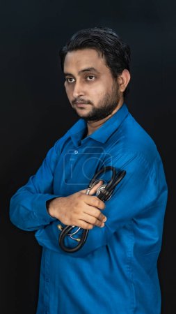 Photo for South Asian Young Male Doctor Holding A Stethoscope On Shoulder Isolated On Black Background, Portrait Of Medical Professional, Copy Space On Both Side - Royalty Free Image