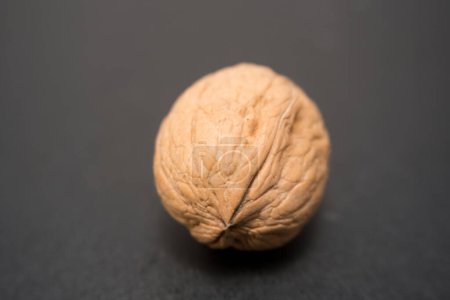 Simplicity and Elegance: A Single Walnut on a Dark Surface, This image features a single, uncracked walnut, its intricate textures beautifully highlighted against a dark grey background.