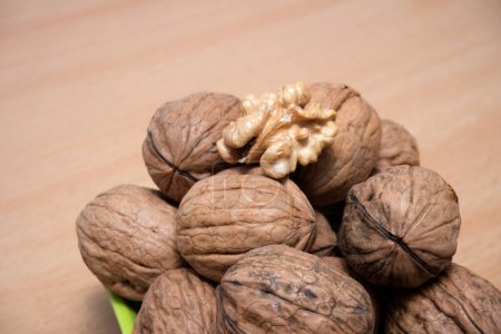 Fresh, Organic Walnuts on a Smooth Wooden Surface, This image beautifully captures a group of fresh, organic walnuts, some still in their hard, textured shells and one cracked open to reveal