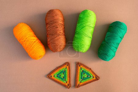 Photo for Two crochet motifs in green and orange tones and four skeins of yarn in same colors on beige background. Crochet and yarns concept. - Royalty Free Image