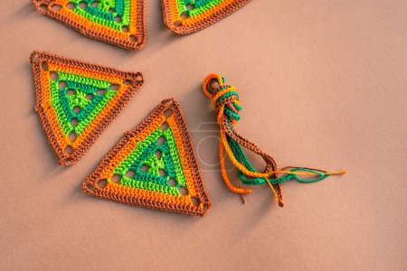 Photo for Some multicolored triangle crochet motifs and a bundle of multicolored crochet cords on beige background. Concept of crocheting in green and orange tones. - Royalty Free Image