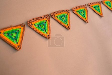 Téléchargez les photos : Ligne diagonale de morceaux de triangle au crochet dans les tons orange et vert sur fond beige. Crochet triangle drapeaux. - en image libre de droit