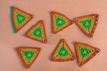 Photo for Seven multicolored crochet motifs on beige background. Hand made crochet pieces in green and orange tones. - Royalty Free Image