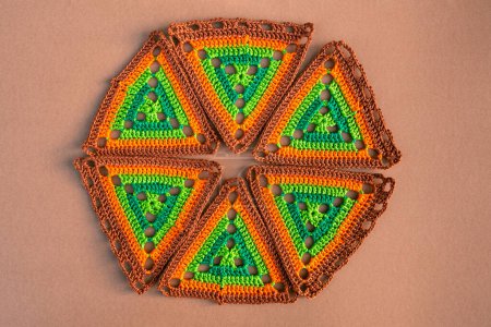 Photo for Round figure made of crochet triangles in green and orange tones on beige background. Concept of creative crocheting. - Royalty Free Image